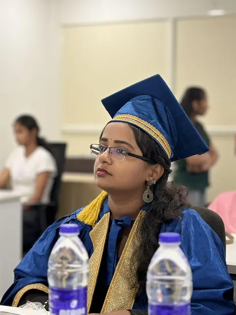 A graduate in a blue robe and cap seated at the ceremony